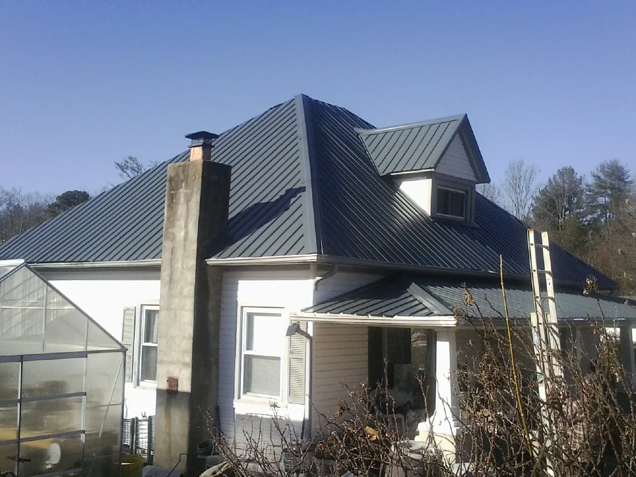 Dark blue standing seam metal roof on a white farmhouse with dormer — Slate & Tile Roof Repair by Roofing Brothers in Longboat Key