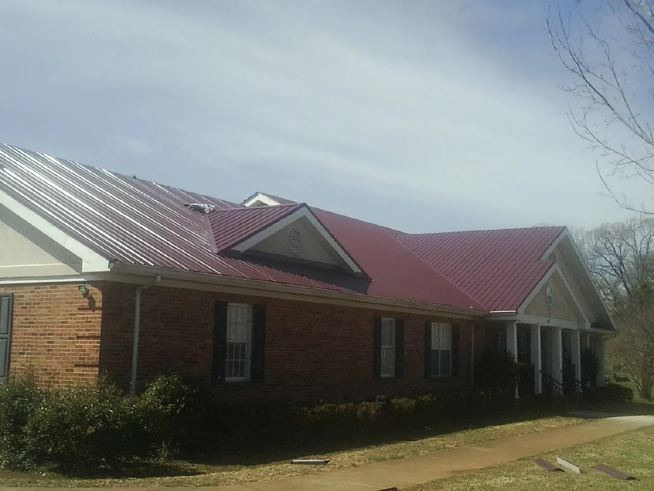 Red metal roof with gabled entries on a long brick building, from a Hail Damage Roof Repair job in Longboat Key