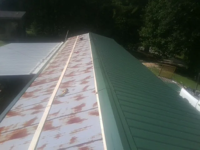 Old rusted panels beside newly installed green metal roofing — Wind Damage Roof Repair by Roofing Brothers in Longboat Key