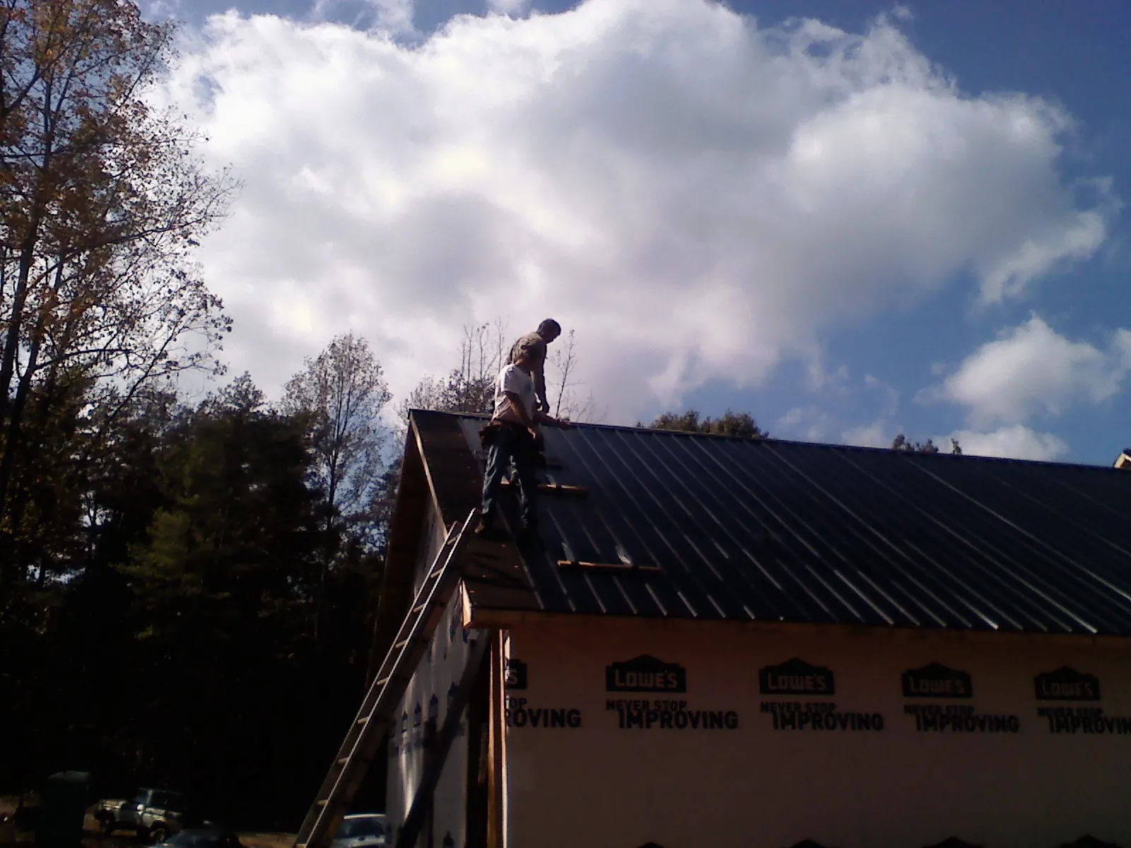Roofer fastening dark metal panels high against a cloudy sky, from a Roof Inspection job in Longboat Key