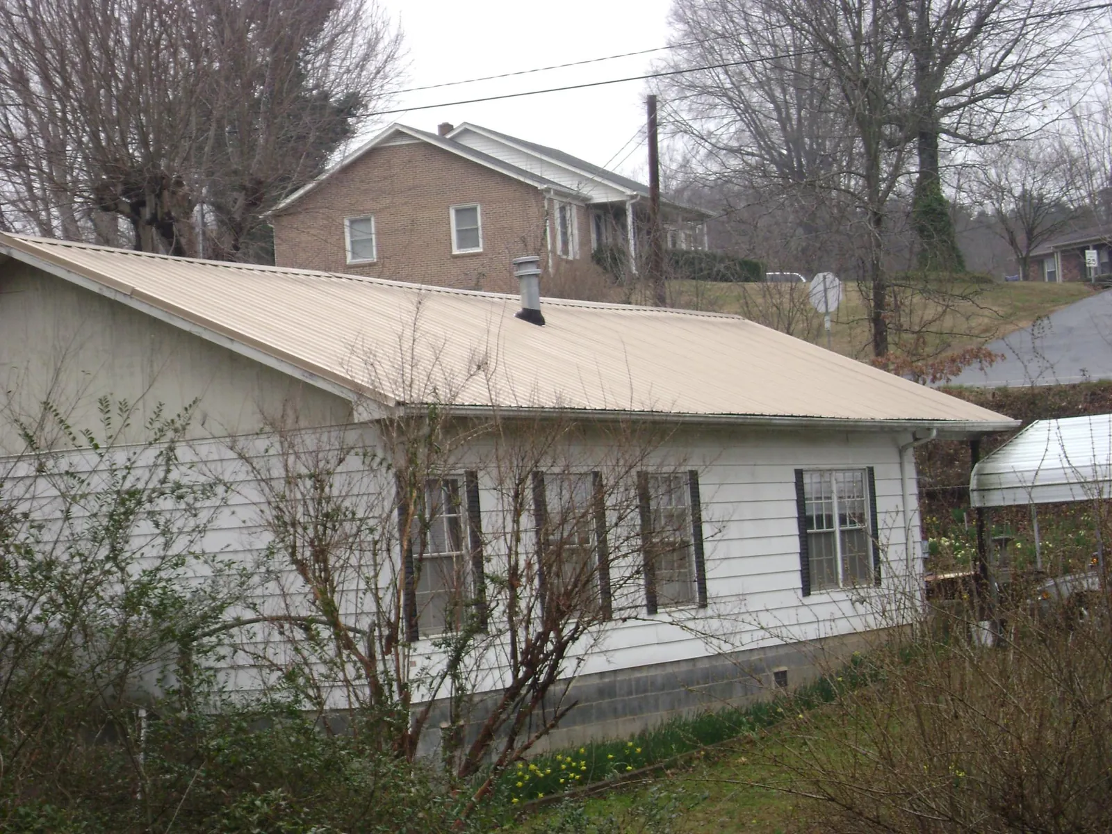 Tan metal roof on a white sided house set into a hillside — Commercial Roofing by Roofing Brothers in Longboat Key