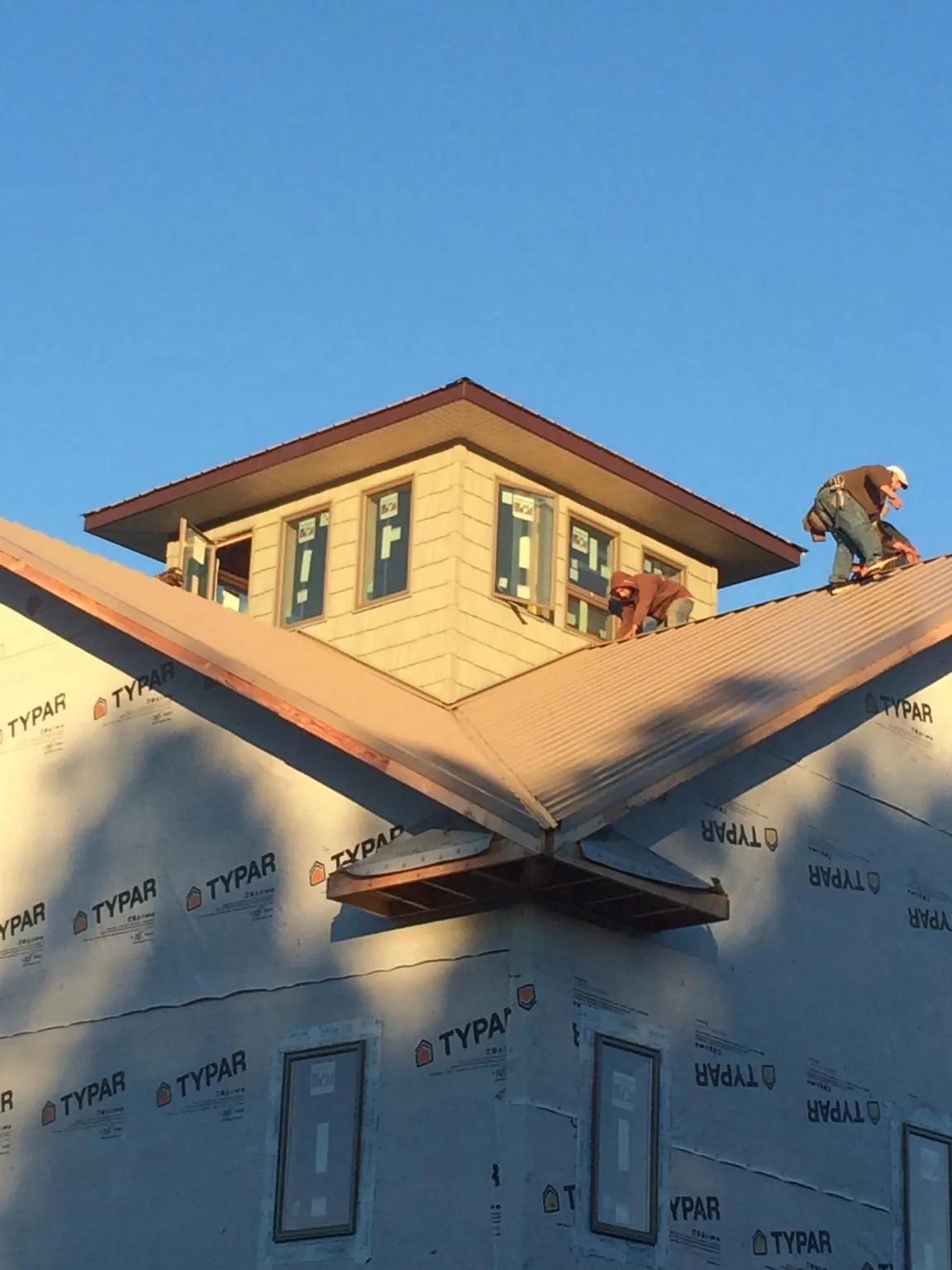 Roofers working around a rooftop cupola on a new metal roof at sunset in Longboat Key